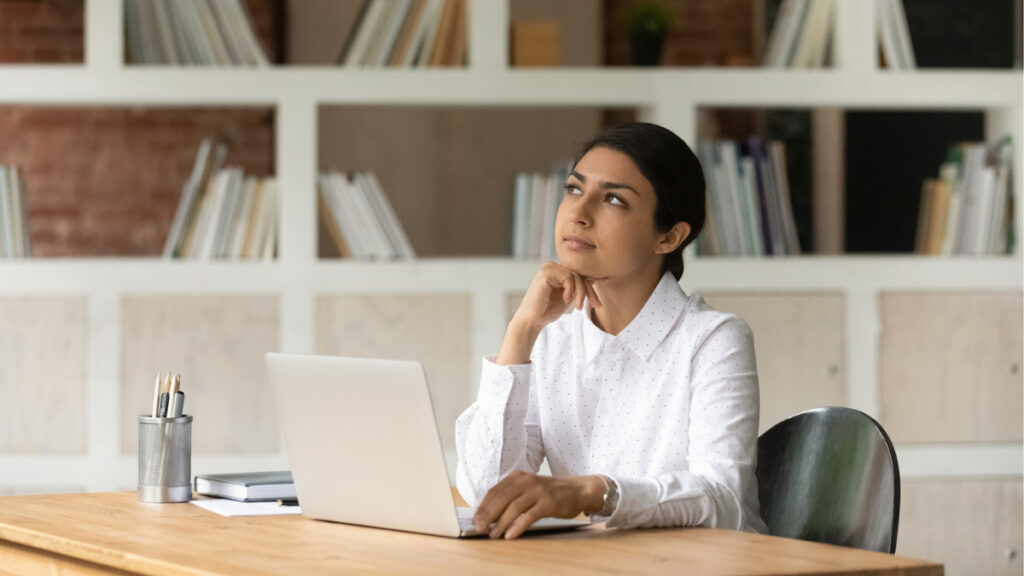 Woman looking thoughtful in an office with laptop